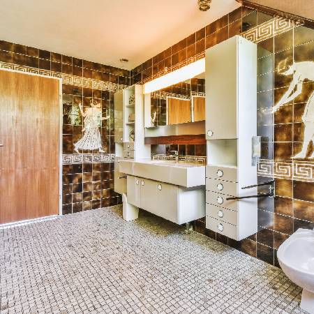 Retro bathroom with brown and white geometric tiles, a large mirror, and built-in vanity unit. Greco-Roman motifs decorate the walls.