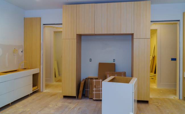 A partially completed kitchen with light wood cabinets, an empty central alcove, and construction materials on the floor.