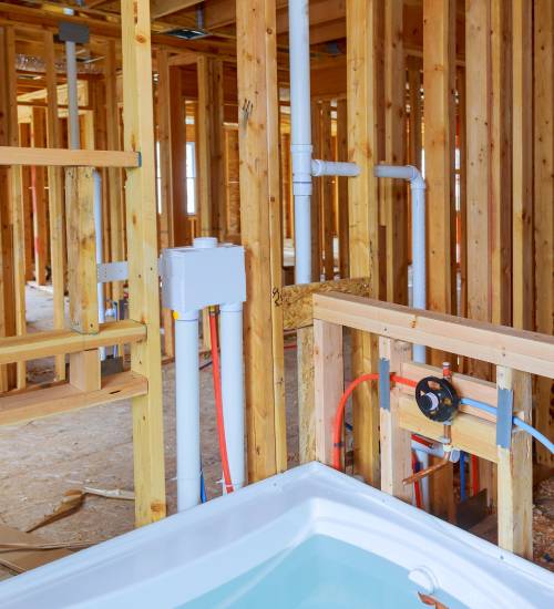 Partially built bathroom with exposed wooden framing and piping, featuring a bathtub with some water inside.