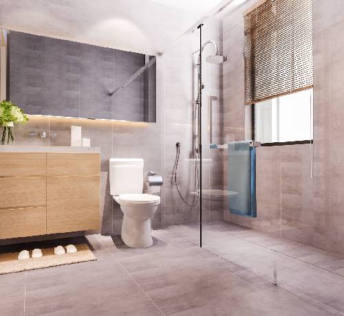 Modern bathroom with a shower, toilet, wooden vanity, large mirror, and a window with blinds. The space has light gray tiles and a blue towel on a glass divider.