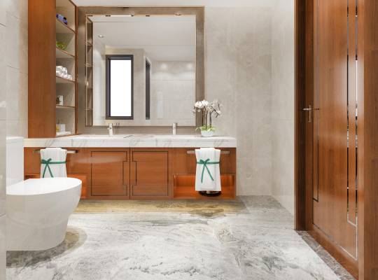 Modern bathroom with wooden cabinets, marble countertops, dual sinks, and a large mirror. Toilet on the left, neatly folded towels with green ribbons, and decorative orchids on the counter.